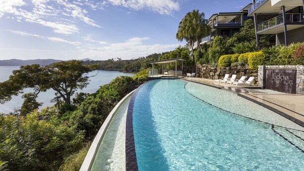 Una piscina con agua azul cristalina, rodeada de abundante vegetación y con vistas a un cuerpo de agua.