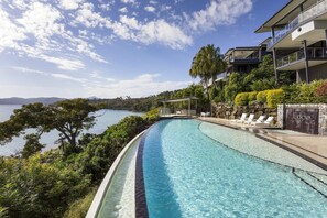 A swimming pool with clear blue water, surrounded by lush greenery and overlooking a body of water.