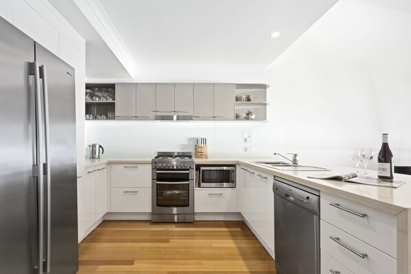 A modern kitchen with stainless steel appliances, white cabinetry, and a wooden floor.