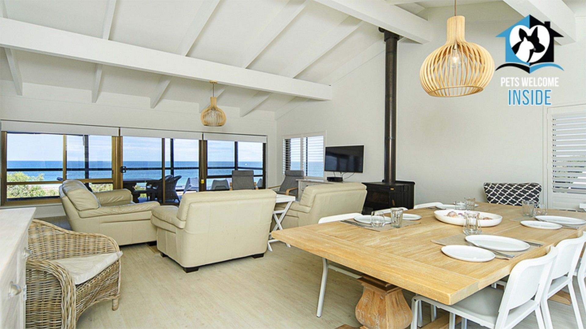 A spacious living area with a large wooden dining table, comfortable seating, a television, and a view of the ocean.