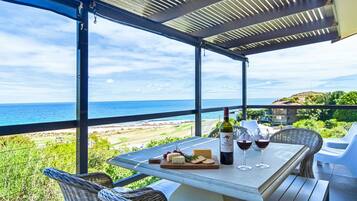 A covered outdoor seating area with a table set for two, overlooking a beach and ocean view.