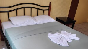 Ein ordentlich gemachtes Bett mit weißen Kissen und einem gefalteten Handtuch auf einer hellgrünen Bettdecke.
