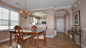 Un comedor con una mesa y sillas de madera, una lámpara de araña y vistas a la cocina a través de un arco.