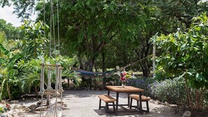 Ein Holztisch mit Bänken in einem Garten, eine Hängematte und Reckschaukeln.