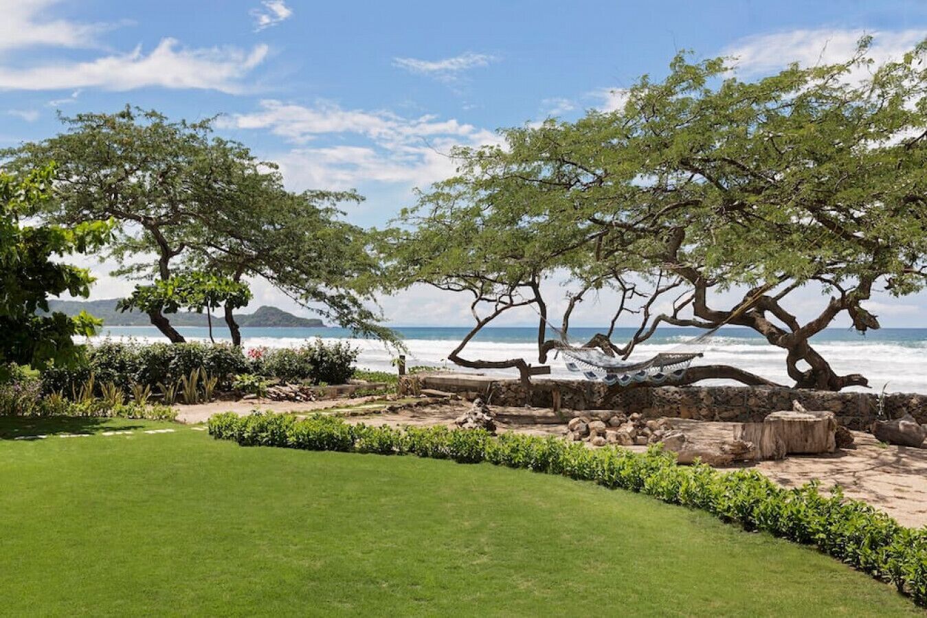 A coastal garden with a grassy lawn, a hammock, and a stone wall.
