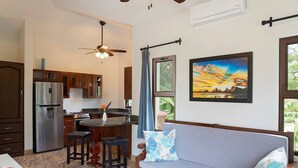 Eine moderne Küche mit Kühlschrank, Herd und Essbereich. Ein Sofa mit Kissen und ein Bild an der Wand sind ebenfalls vorhanden.