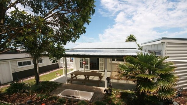 A residential property with a covered patio, a small garden with a palm tree, and a wooden bench.