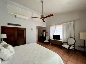 Camera d'albergo con un letto, una scrivania con computer, una TV, una ventola a soffitto e una finestra con tende.
