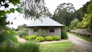 A small, single-story house with a sloped roof, surrounded by well-maintained gardens and trees.