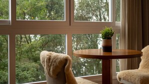 A room with large windows, a round wooden table, a potted plant, and a fluffy chair. - Comfort and Nature 1.2km from the Center of Gramado (Gramado)