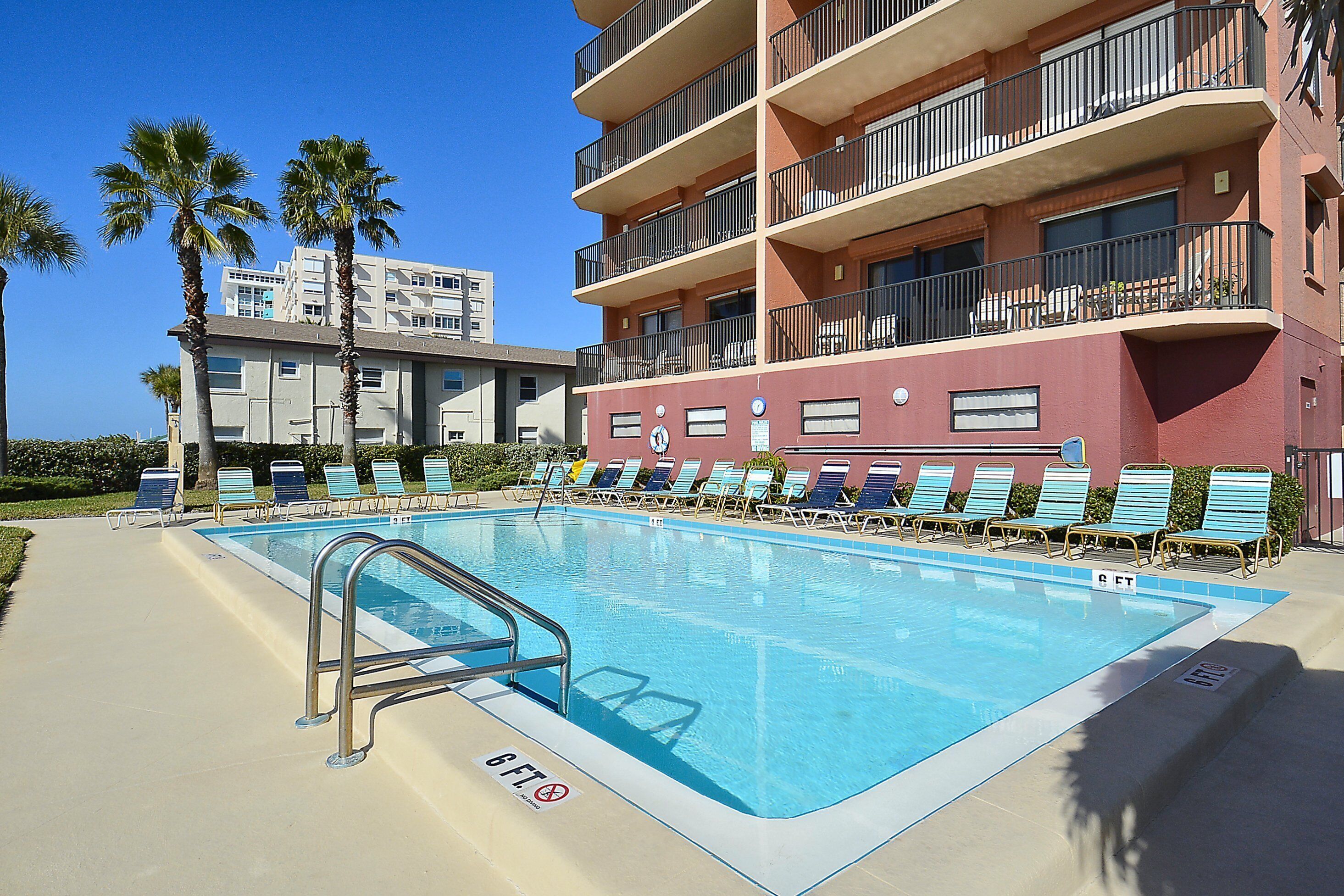 Una piscina con un indicador de profundidad de 6 pies, rodeada de sillas de descanso y un edificio con varios balcones.