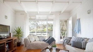Ein geräumiges Wohnzimmer mit großem Fenster, einer Sofagarnitur, einem Couchtisch mit Tablett und einem Fernseher.