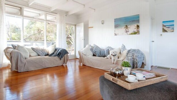 Ein geräumiges Wohnzimmer mit Holzboden, zwei Sofas, einem Couchtisch mit Tablett und einem großen Fenster mit Vorhängen.