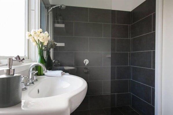 Casa de banho moderna com azulejos escuros, uma sanita branca, um espelho e um vaso com flores.