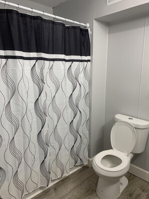 Une salle de bain avec des toilettes blanches, un rideau de douche à motifs noirs et blancs, et un plancher en bois.