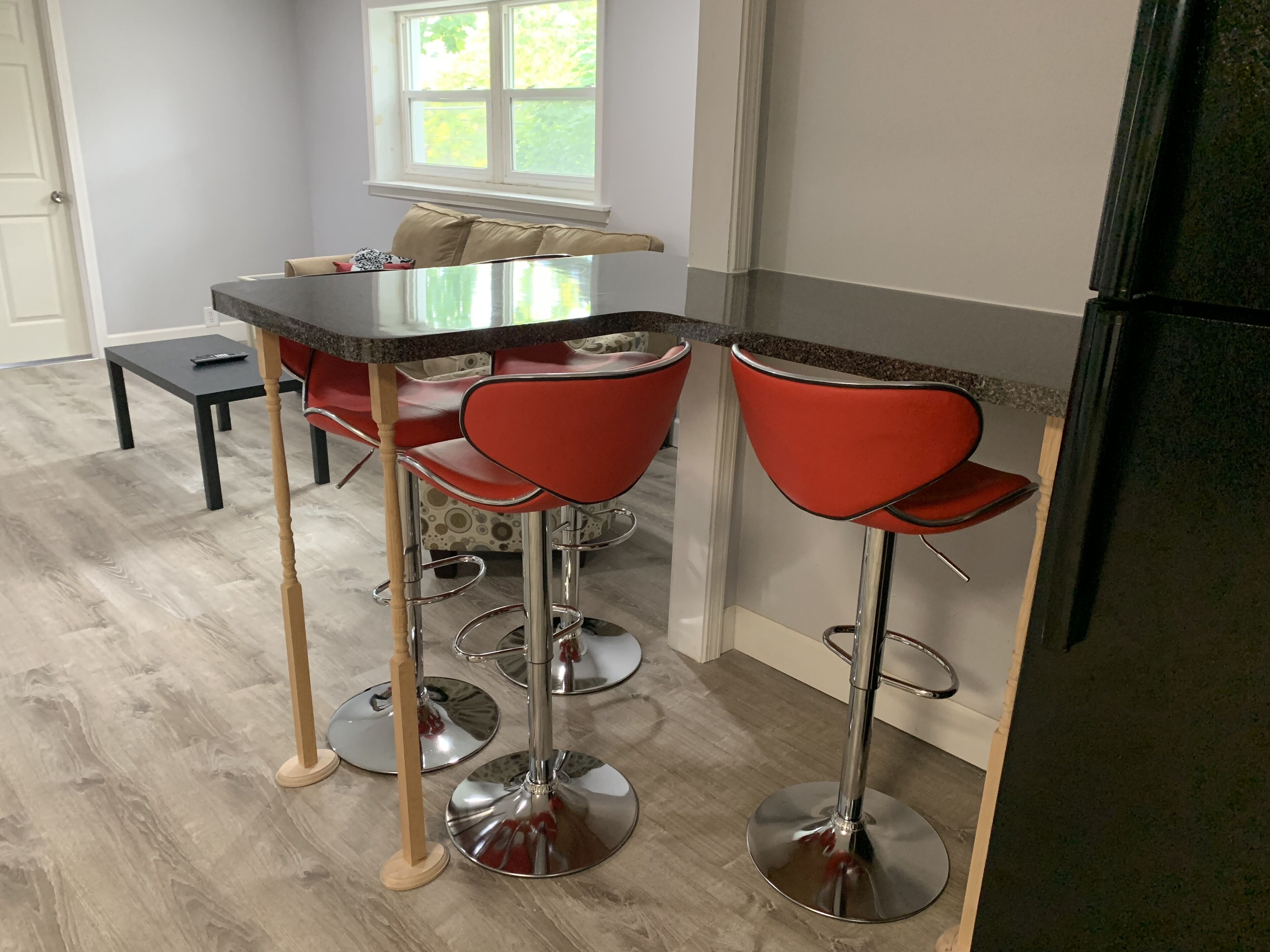 Una cocina con barra, que incluye taburetes rojos, una encimera negra y un refrigerador de acero inoxidable.