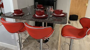 Cocina compacta con un refrigerador negro, una mesa de comedor con platos y vasos rojos, y cuatro taburetes altos rojos.