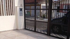 Un área cercada con suelo de baldosas, un cuadro de electricidad y un edificio con tejado de tejas rojas al fondo.