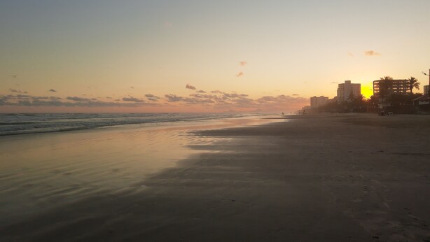 Una playa con un atardecer, edificios y un cielo despejado.