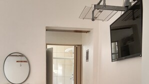 Un pasillo con un espejo, una estantería, una puerta que da al baño y un televisor montado.