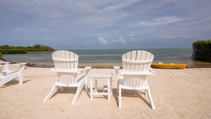 Ein Strand mit weißen Adirondack-Stühlen und einem gelben Boot im Sand.