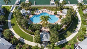 Ein Luftbild eines Resorts mit einem zentral gelegenen Schwimmbad, umgeben von Palmen und Liegestühlen.