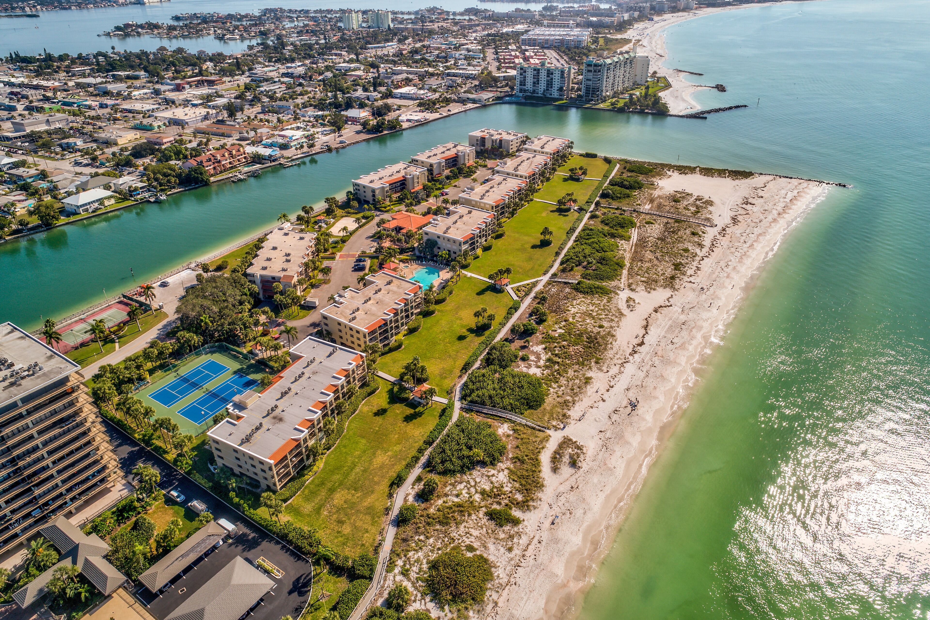 Vista aérea de una zona residencial costera con un puerto deportivo, cancha de tenis y una playa.