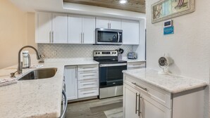 Una cocina compacta con gabinetes blancos, un microondas de acero inoxidable, una estufa y un lavabo.