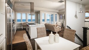 A spacious kitchen with a large island, a dining area with wicker chairs, and a view of the ocean through large windows. - Luxury Oceanfront Escape with Unobstructed Ocean Views (York Beach)