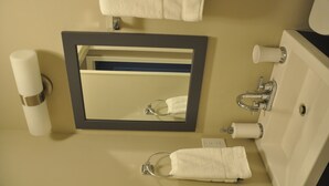 Een badkamer met een wastafel, spiegel, handdoekhouder en toiletpapierhouder.