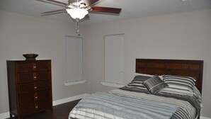Een slaapkamer met een bed, een dressoir, een plafondventilator en ramen.