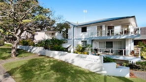 Uma casa de dois andares com fachada branca, uma varanda no andar superior e um gramado bem cuidado.