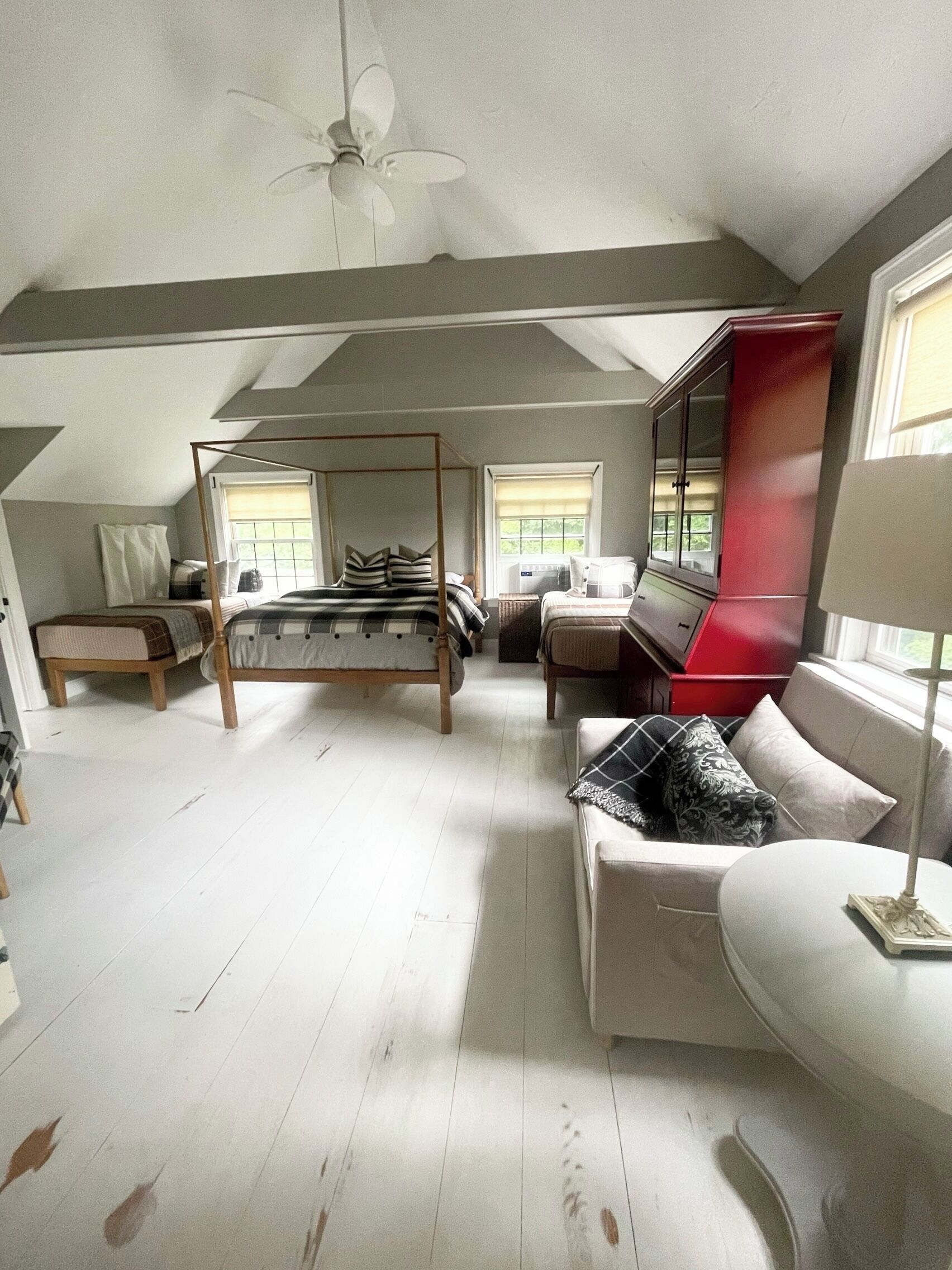 A bedroom with a four-poster bed, a sofa, a red cabinet, and a ceiling fan.