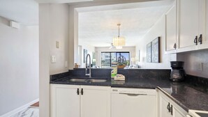 A modern kitchen with white cabinets, a black countertop, and a dishwasher. - Land's End 303 Bldg 5~ Unique Water Views, Pool (Treasure Island)