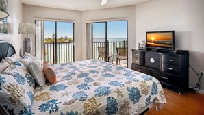 A bedroom with a bed, a television, a dresser, and a balcony with a view of the ocean. - Land's End 303 Bldg 5~ Unique Water Views, Pool (Treasure Island)