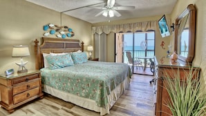 Un dormitorio con cama, mesitas de noche, cómoda, ventilador de techo y balcón con vistas.