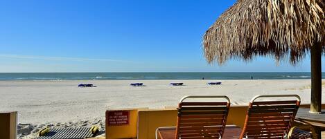 A beachside seating area with lounge chairs and a thatched umbrella, overlooking the beach.