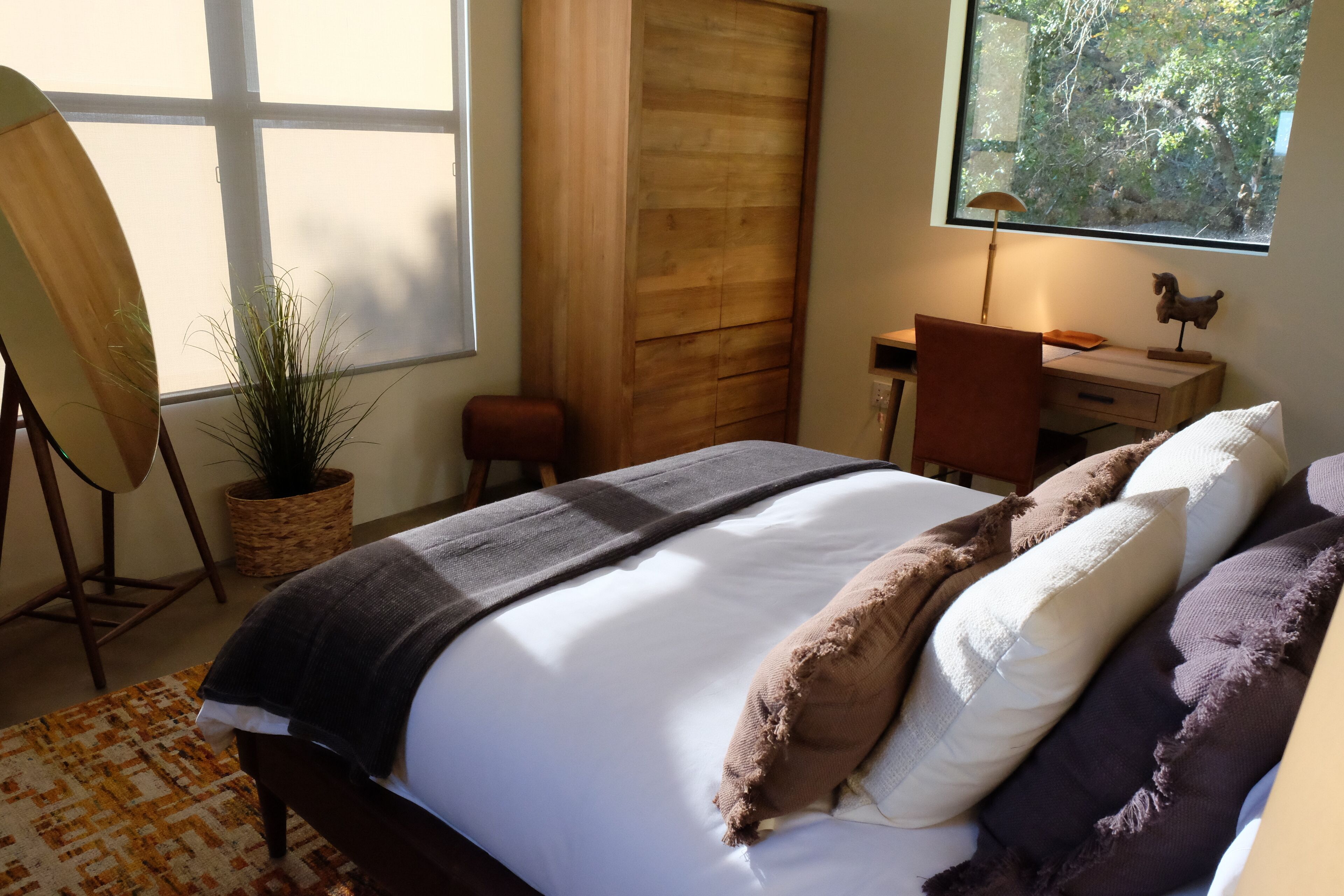 Un dormitorio con una cama, un escritorio, una silla, una planta en maceta y un ventanal con vistas a árboles.