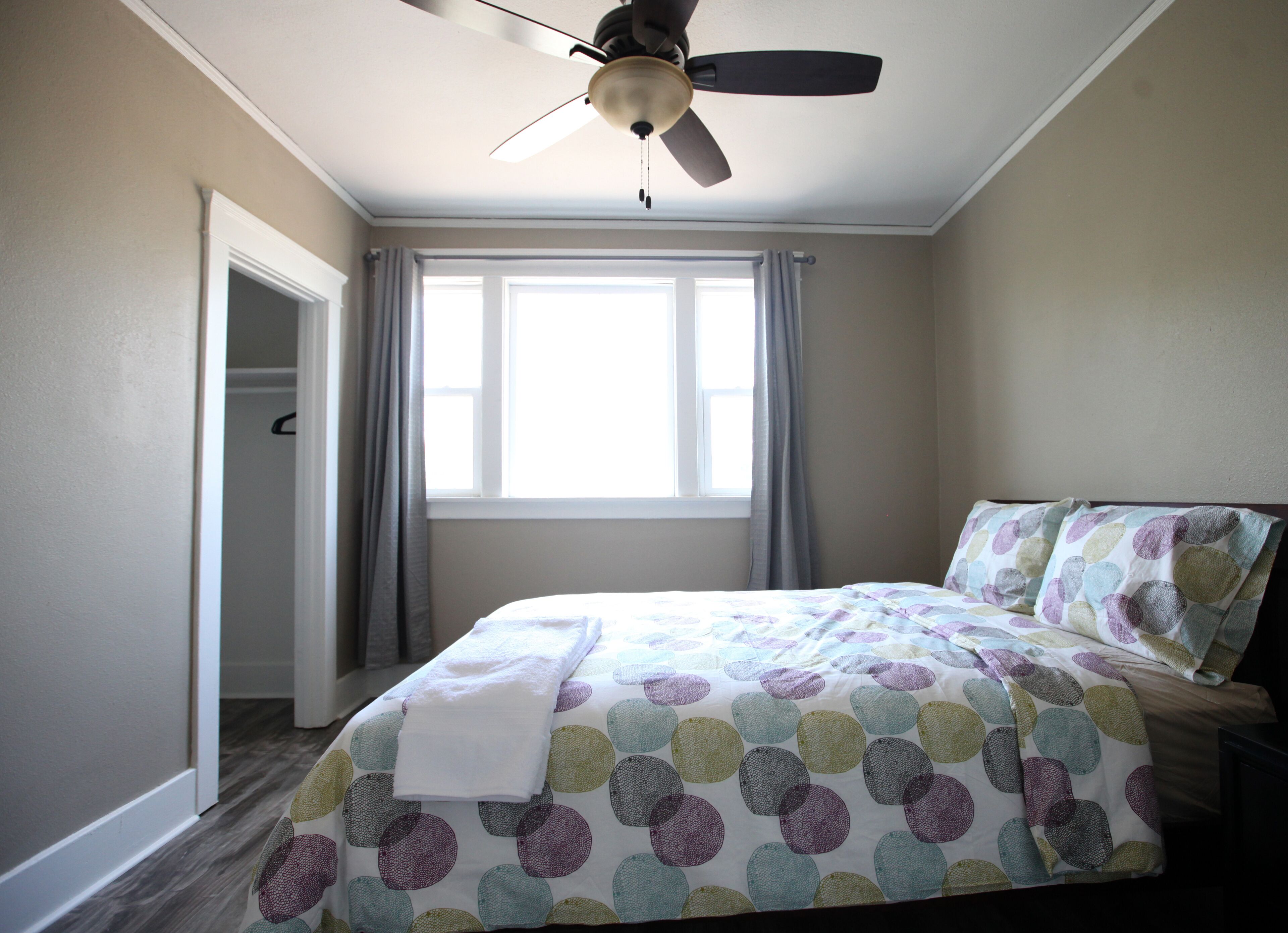 A bedroom with a bed, a ceiling fan, a window with curtains, and a door.