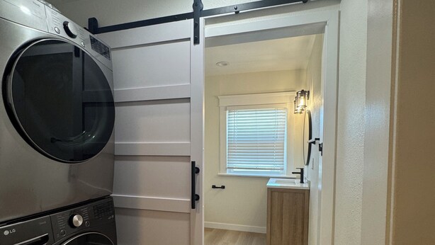 A laundry area with a front-loading washer and dryer, a sliding door leading to a bathroom, and a small window with blinds. - 3 Br Disneyland Home — Sleeps 6-8 (Anaheim)