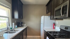 A modern kitchen with dark cabinets, stainless steel appliances, and a tiled floor. - 3 Br Disneyland Home — Sleeps 6-8 (Anaheim)