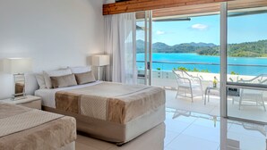 A modern hotel room with a large bed, a smaller bed, and a balcony with white wicker furniture. - Bella Vista East 9: 2 bedroom oceanview apartment with golf buggy (Hamilton Island)