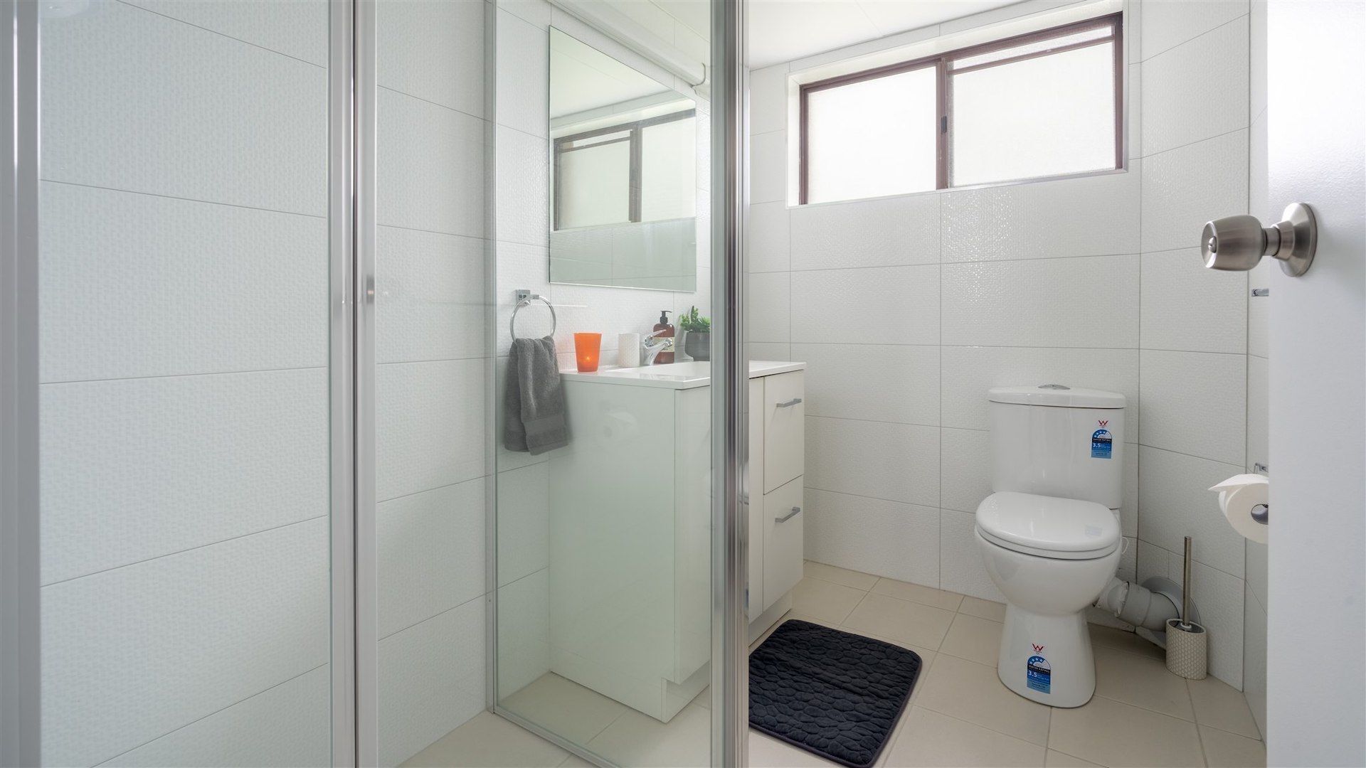 A modern bathroom with a glass shower enclosure, a toilet, a sink, and a small window.