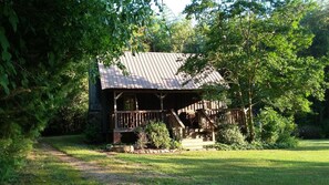 Une cabane rustique dotée d’une terrasse en bois et d’un toit en métal, entourée d’une végétation luxuriante.