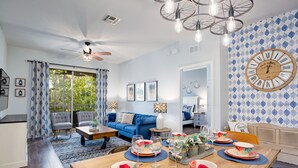 Een moderne woonkamer met een blauwe bank, een eettafel gedekt voor een maaltijd, en een grote wandklok.