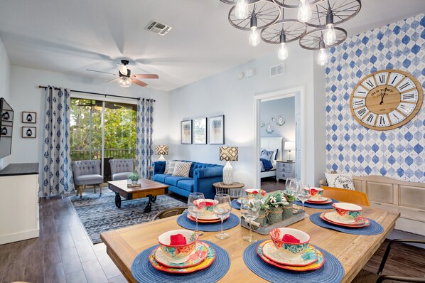 Una sala de estar moderna con un sofá azul, mesa de comedor lista para una comida y un reloj de pared grande.
