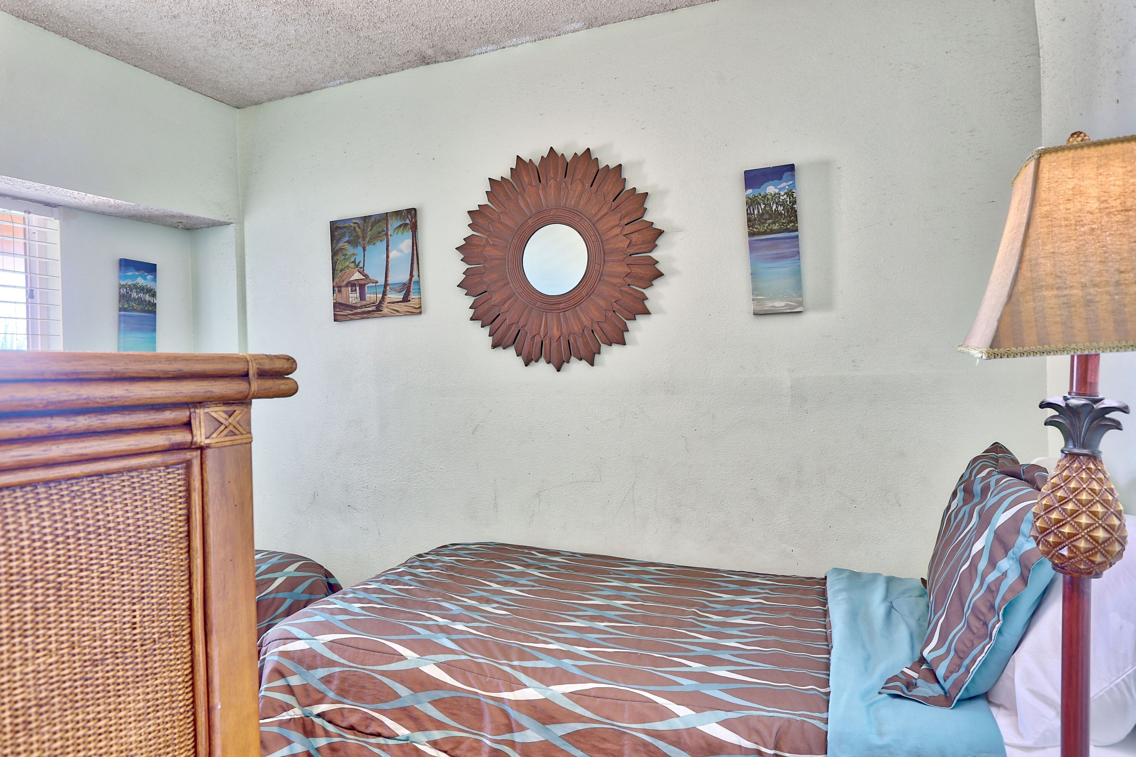 Une chambre à coucher avec un lit, un miroir fixé au mur et une fenêtre avec des stores.