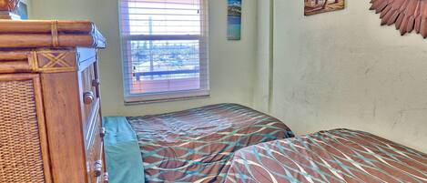 A bedroom with two beds, a window with blinds, and a wall-mounted mirror.