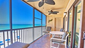 A balcony with a view of the ocean, a table, chairs, and ceiling fans.