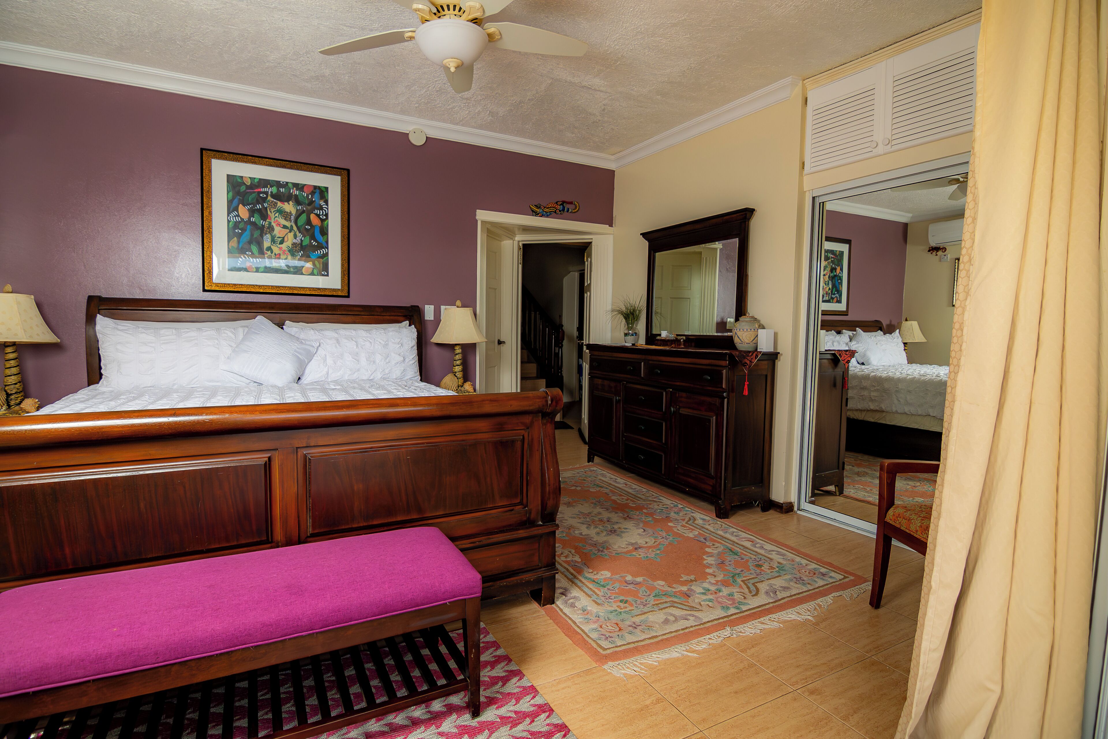 A bedroom with a wooden bed, a bench, a dresser, and a mirror.